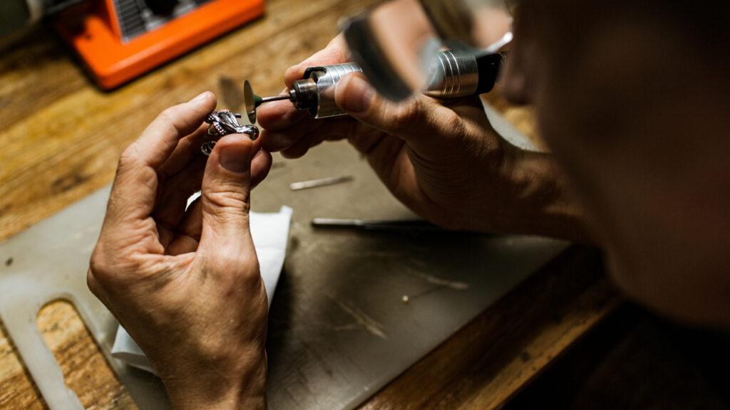 Jeweler using a rotary tool to polish a ring at a small business workshop bench