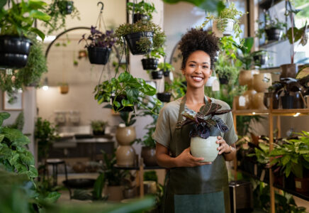 Smiling plant shop owner holding a potted plant in her store, a small business that benefits from working capital solutions to manage inventory and cash flow