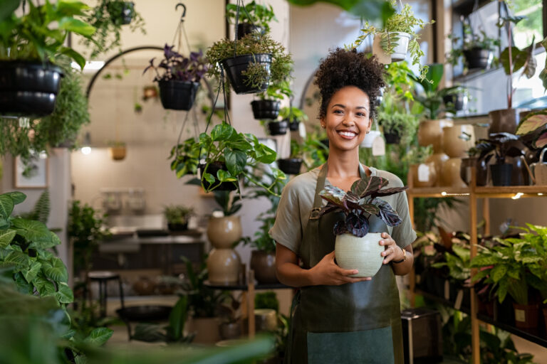 Smiling plant shop owner holding a potted plant in her store, a small business that benefits from working capital solutions to manage inventory and cash flow