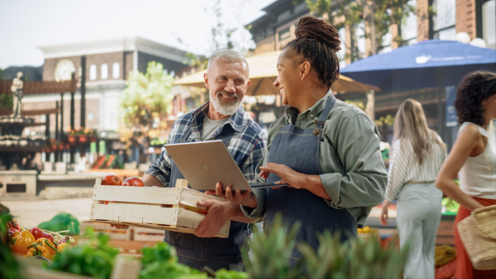 Two small business owners at an outdoor market reviewing their software platform and embedded payment tools on a laptop