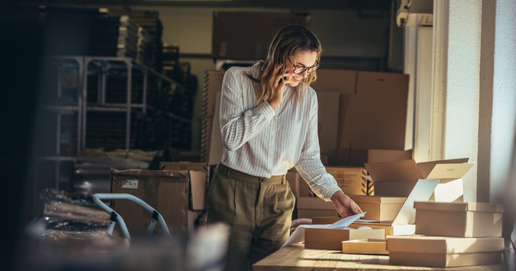 Small business owner on the phone while managing inventory in a warehouse, using working capital to restock and keep operations running smoothly