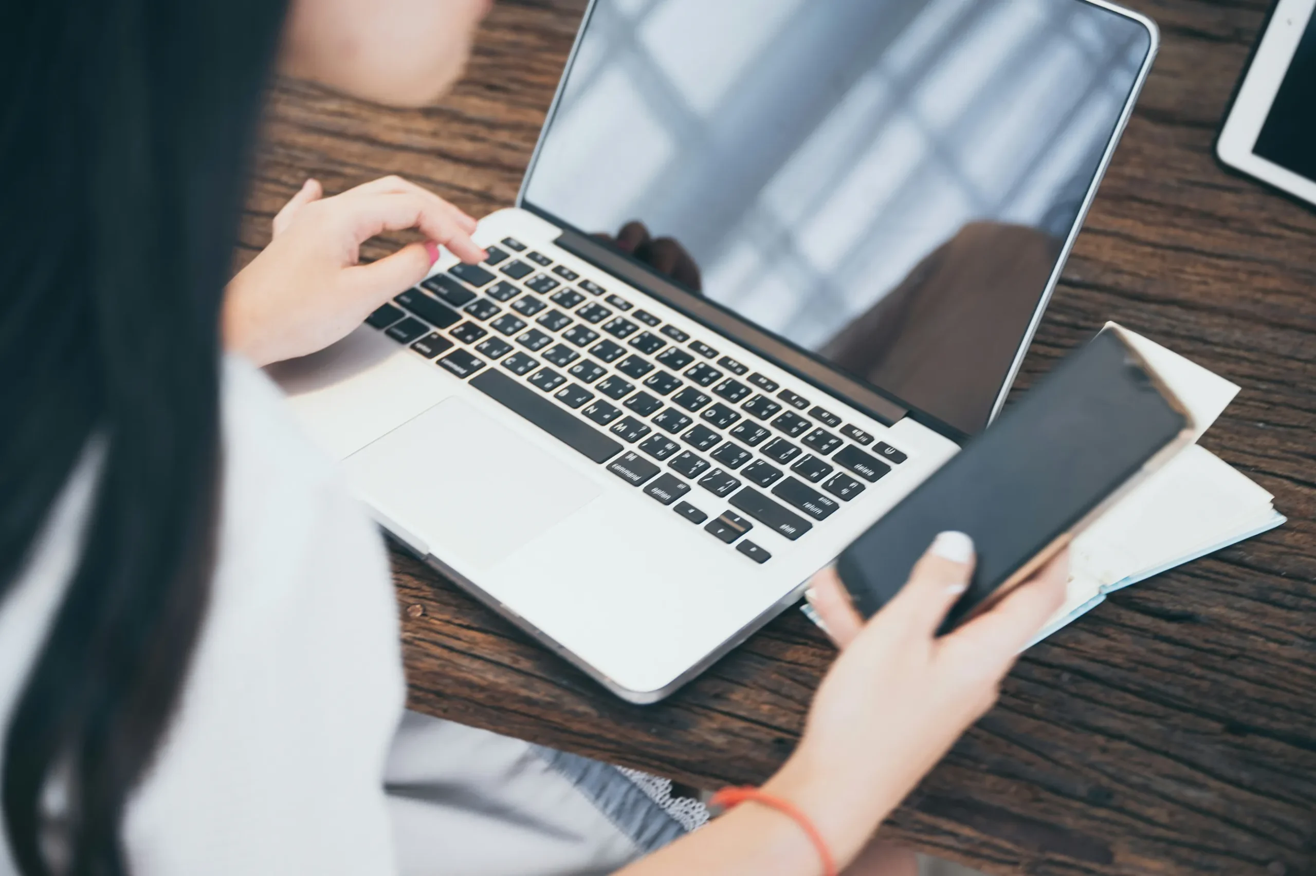 Person typing on a laptop with a credit card and smartphone nearby on a wooden desk, suggesting online shopping or payment