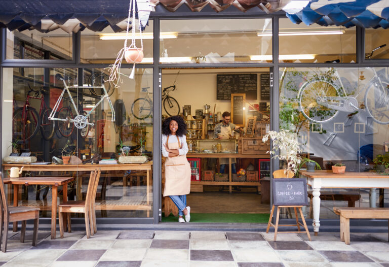 A café owner stands confidently in the doorway of her independent shop, the kind of local business that competes with larger chains on the speed and flexibility of its checkout.