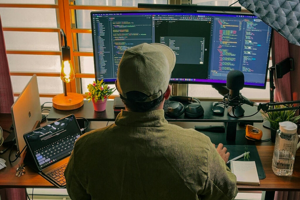 7 Questions to Help You Find the Right Embedded Payments Provider 2 A developer works at a dual-monitor coding station, surrounded by screens displaying code — representing the hands-on build experience SaaS teams should expect from a strong embedded payments partner.