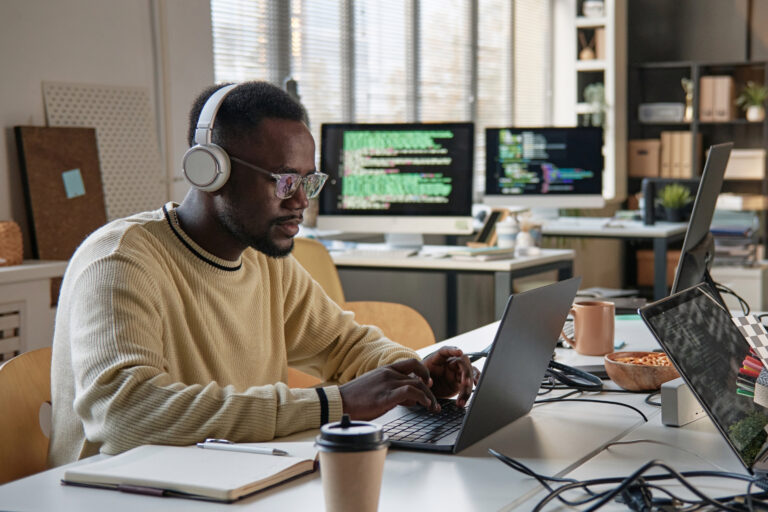 A developer wearing headphones works across multiple code-filled monitors, illustrating the technical integration work at the center of embedding payments into a SaaS platform.