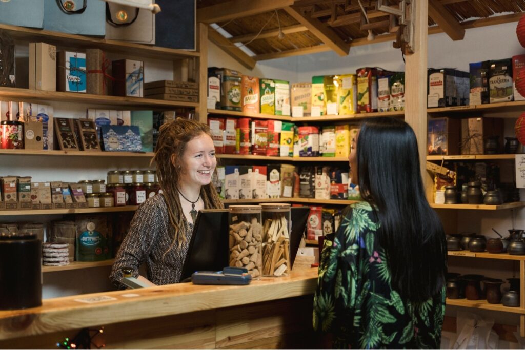 What Are Merchant Services? A Small Business Owner’s Guide to Getting Paid 2 Small business owner accepting a card payment from a customer at a specialty shop counter using a merchant services point-of-sale terminal