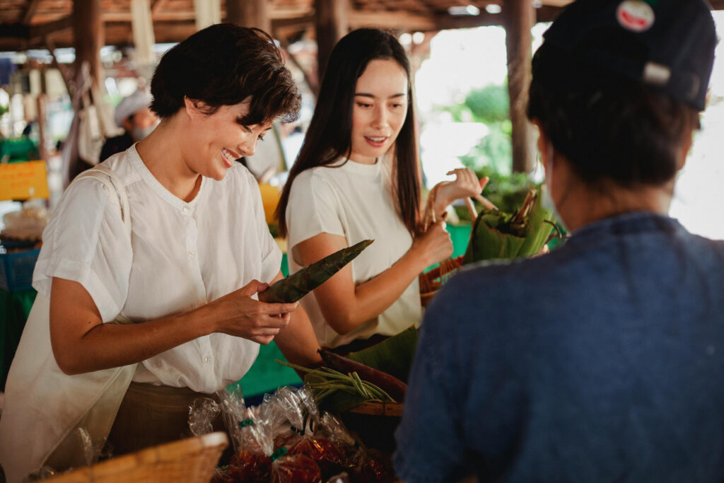 One Bad Payment Experience Is All It Takes: What New Data Reveals 2 Two shoppers smile as they buy fresh produce from a local market vendor, the moment of connection that a frustrating payment experience can quietly undo.