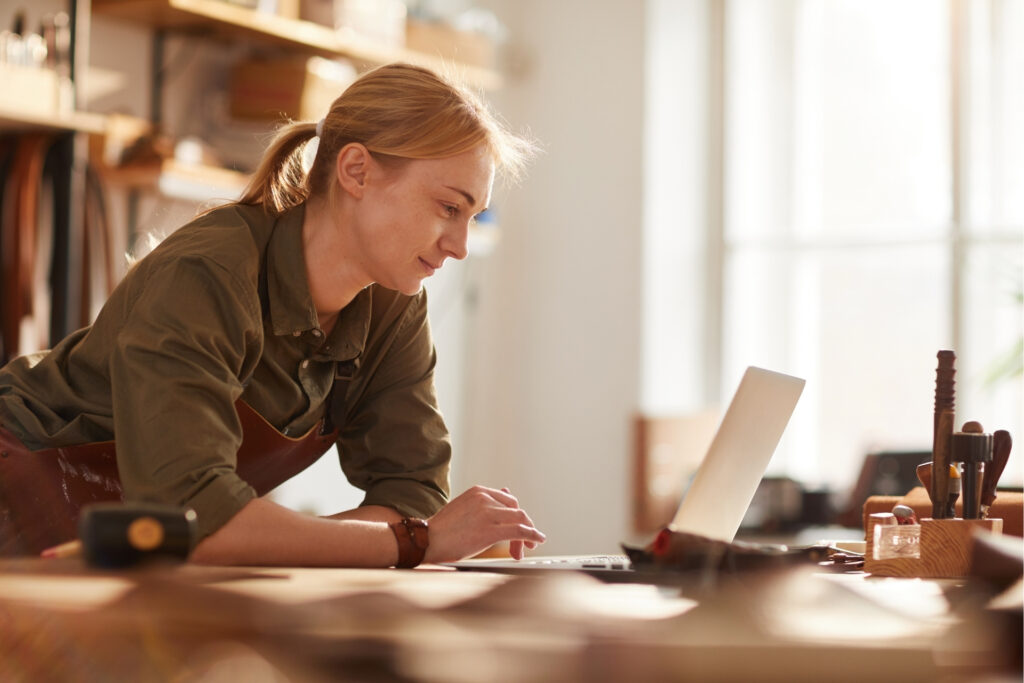 Small business owner reviews her finances on a laptop in her crafts studio, exploring funding options for her growing business.
