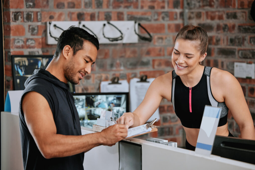 Recurring Payments: A Guide to Steadier Business Revenue 2 A smiling gym employee helps a member fill out a sign-up form for a monthly membership at the front desk.