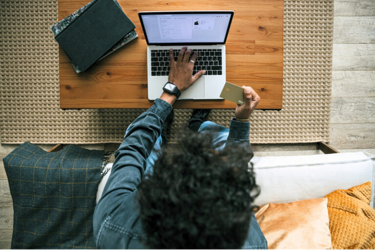 Overhead view of a shopper holding a credit card while completing an online purchase with the help of AI agents on a laptop.