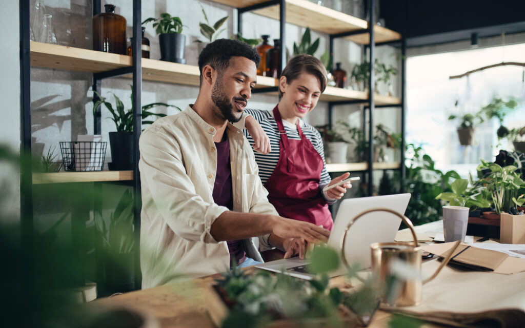 Two small business owners review products that an AI agent found for them on a laptop in their plant shop.