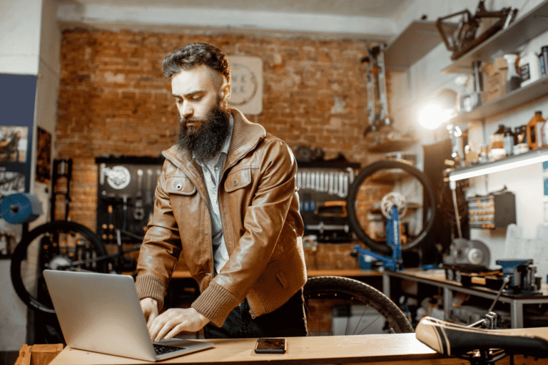 Small business owner reviewing payment reconciliation and cash flow on a laptop at the counter of his bicycle repair shop.
