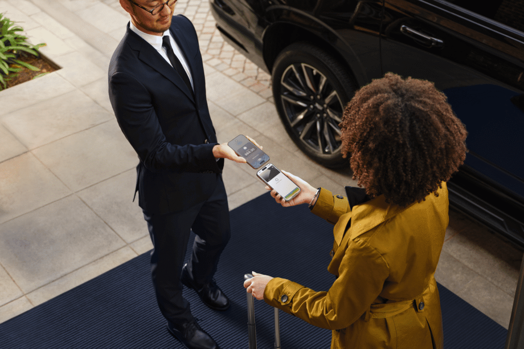 A traveler taps her phone to a hotel attendant's smartphone to pay $64.30 with tap to pay at the hotel entrance.
