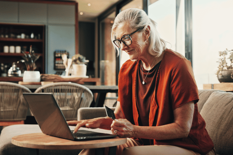 A customer holds her credit card while checking out on a hosted payment page from her laptop in a bright café.